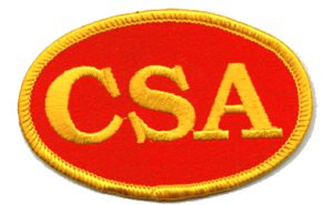 Small CSA iron-on patch with red oval background and yellow embroidered lettering.