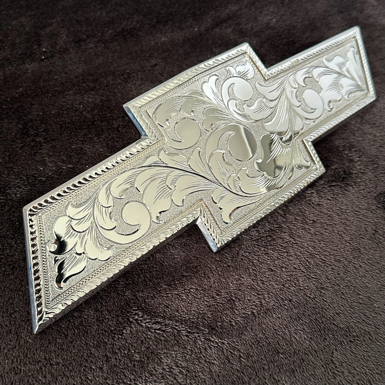 Hand Engraved Chrome Plated Chevy Bowtie
<br> Size: 12" x 4"
<br> Fits Chevy: 
<br> Fits 2014-2015 Model 1500
<br> Fits 2014-2019 Model 2500/3500 H
<br> <br> 
Each piece is hand engraved and has a unique design variation.
<br> No two pieces are the exactly alike.