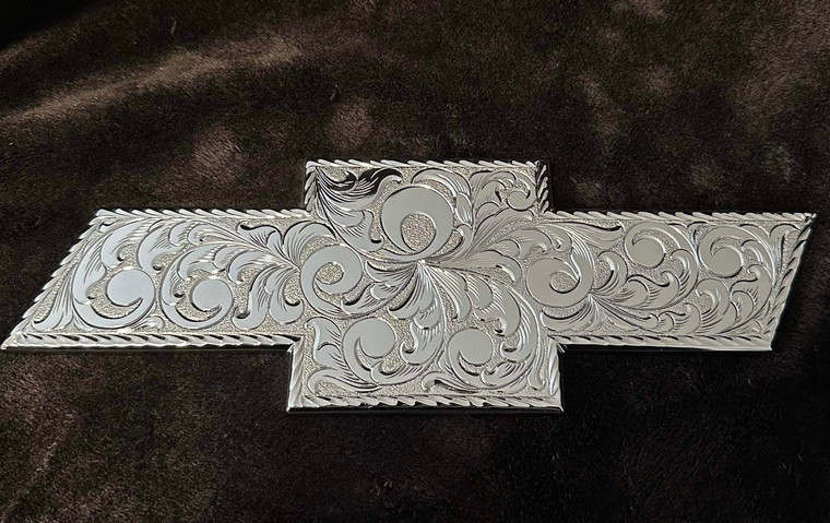 Hand Engraved Chrome Plated Chevy Bowtie
<br> Size: 11.5" x 3.9"
<br> Fits Chevy 2007-2018 Models 1500/2500 HD 
<br> <br> 
Each piece is hand engraved and has a unique design variation.
<br> No two pieces are the exactly alike.