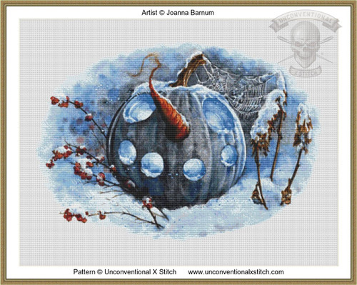 a detailed cross-stitch chart of a winters pumpkin in blue. The blue pumpkin is the central feature in blue with circular holes to make the mouth and two big blue carved out eyes. Surrounding the pumpkin is snow and snow covered berries in red. Atop the pumpkin is a snow covered spiders web.