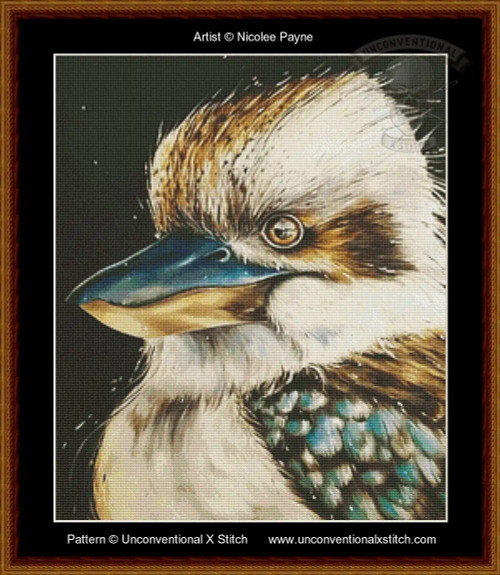A cross-stitch pattern of a kookaburra, focusing on its head. The bird's feathers are rendered in intricate detail with shades of brown, white, and blue, creating a textured and realistic appearance. Its eye is round and expressive, with a black pupil outlined in white. The beak is prominent, colored in a gradient from dark blue to light brown at the tip. The background is a deep black, which contrasts with the bird's light-coloured feathers. 