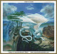 cross stitch pattern of a dragon with blue-white scales and large wings sits on a cliff with carved faces and trees, against a sky with clouds