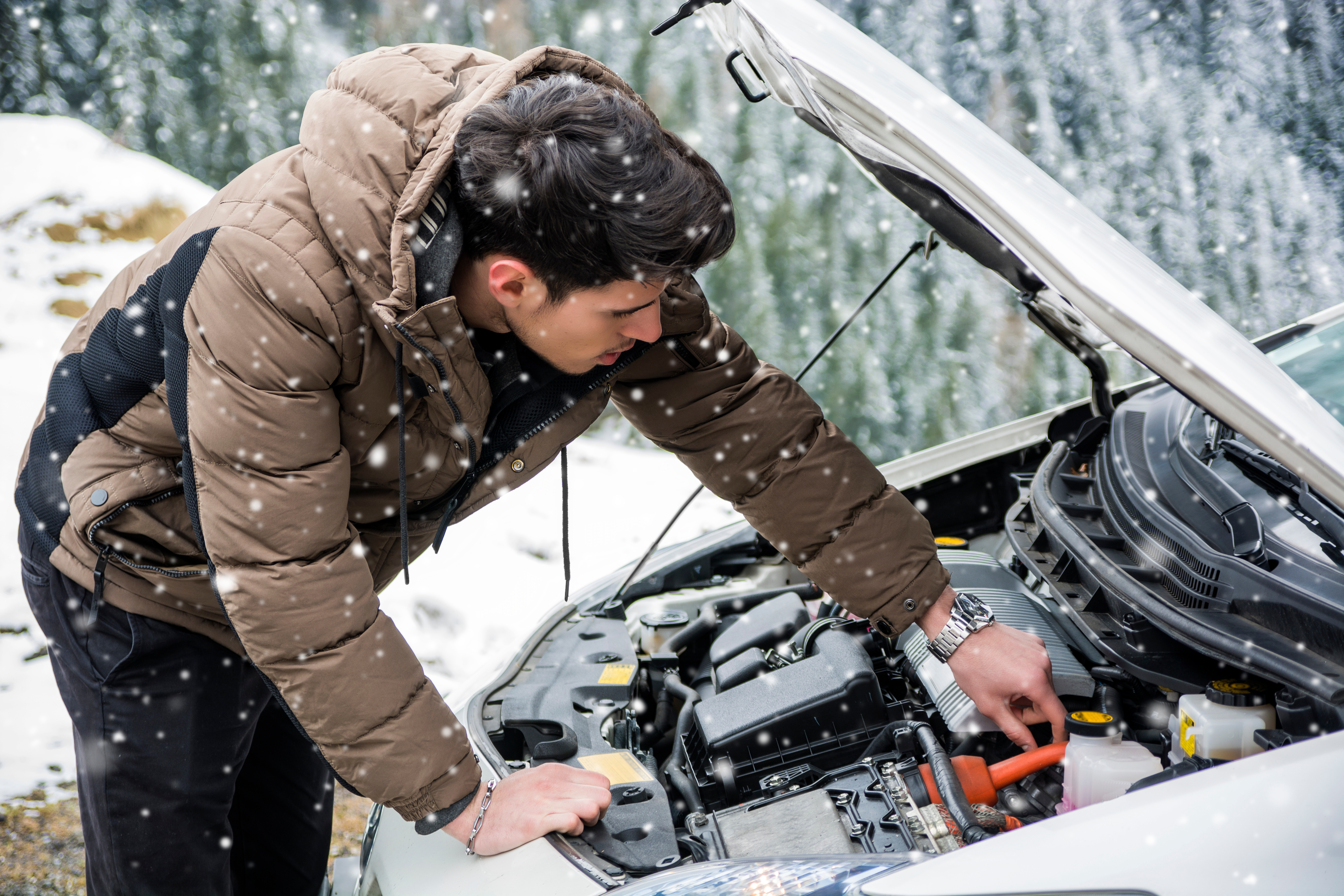 Man checking under the hood of his car with snow falling