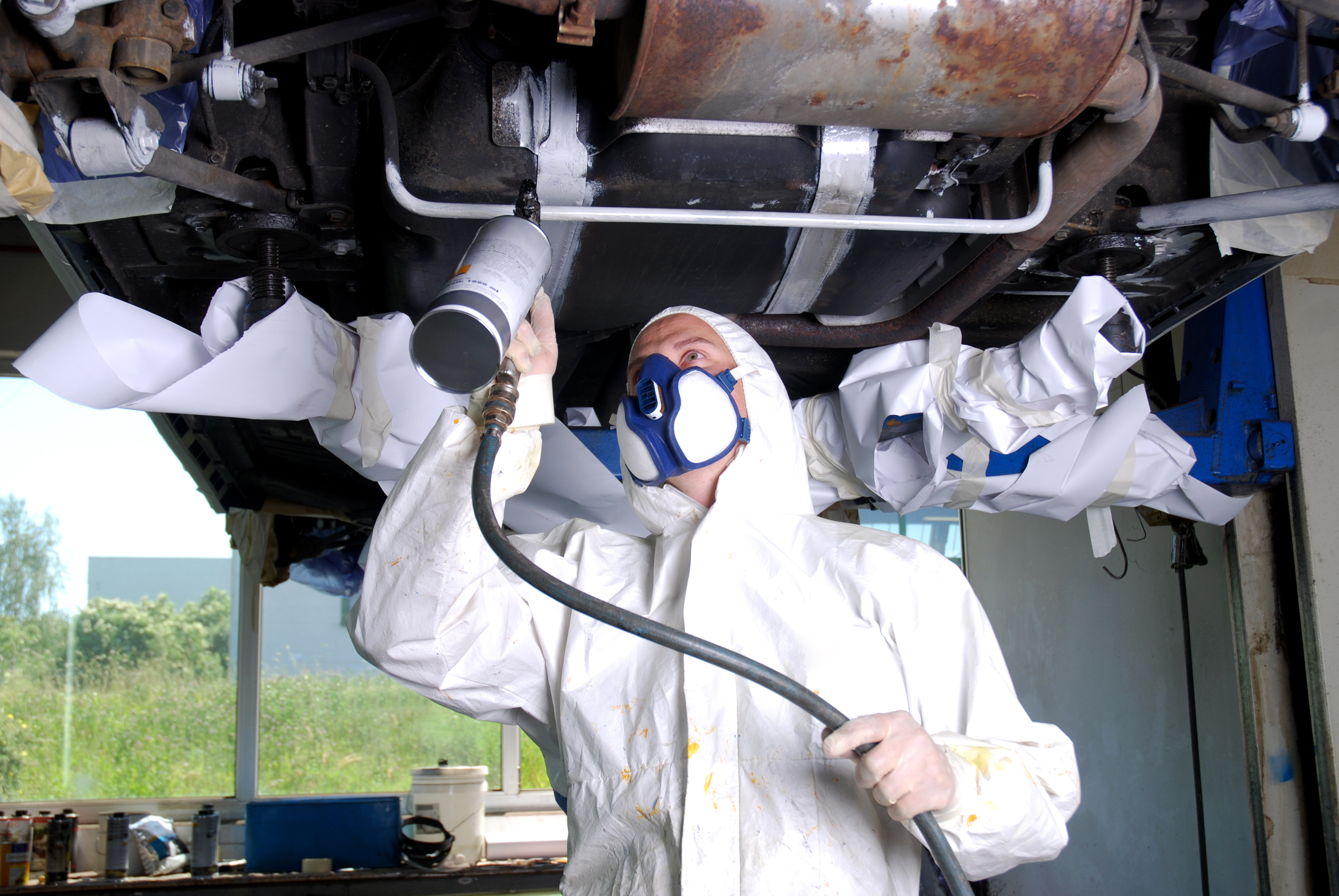 Man in a Tyvek Suit using a spray gun on a vehicle's underbody
