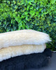 Folded half short wool sheepskin rugs on a garden table, made in New Zealand.