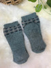 A pair of light gray knitted wool socks with wave trimming., folded and placed on a fluffy white rug.
