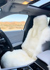 Universal white sheepskin car seat cover installed on a black leather car seat