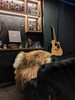 A warm and cosy den for men in rich dark colours, complete with a liquor bar, acoustic guitar and an icelandic sheepskin rug  in natural brown colour draped over a black leather armchair.