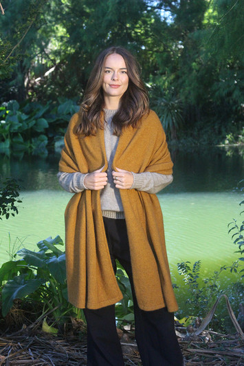 A very large knitted wrap that can be used as an oversized scarf or small blanket, made of possum merino in golden yellow color.