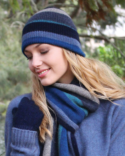 A woman outdoors wearing a blue pullover with matching knitted wool scarf and beanie with wide multicolored stripes. A woman outdoors wearing a blue pullover with matching knitted wool scarf and beanie with wide multicolored stripes.