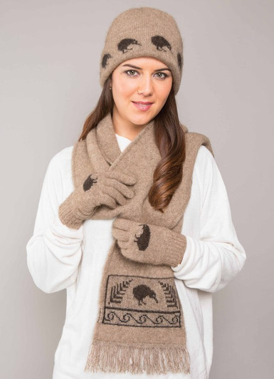 A woman wearing matching knitted wool gloves, scarf and beanie in mocha color with kiwi icons in brown. A woman wearing matching knitted wool gloves, scarf and beanie in mocha color with kiwi icons in brown.