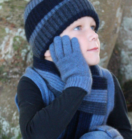 A cute little boy, bundled up in a dark blue pullover with a striped dark and light blue scarf and beanie with matching light blue gloves.