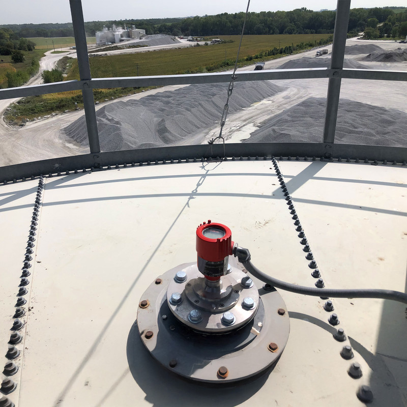 BinMaster 80 GHz non-contact radar sensor mounted atop a bin overseeing large piles used in mining operations 