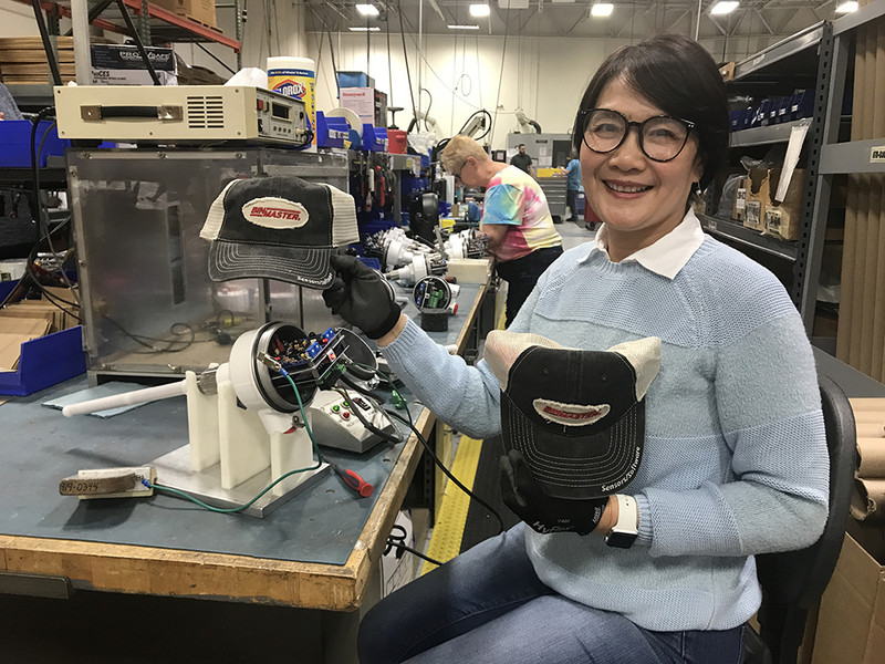 Production line at BinMaster; worker holds a BinMaster-branded hat
