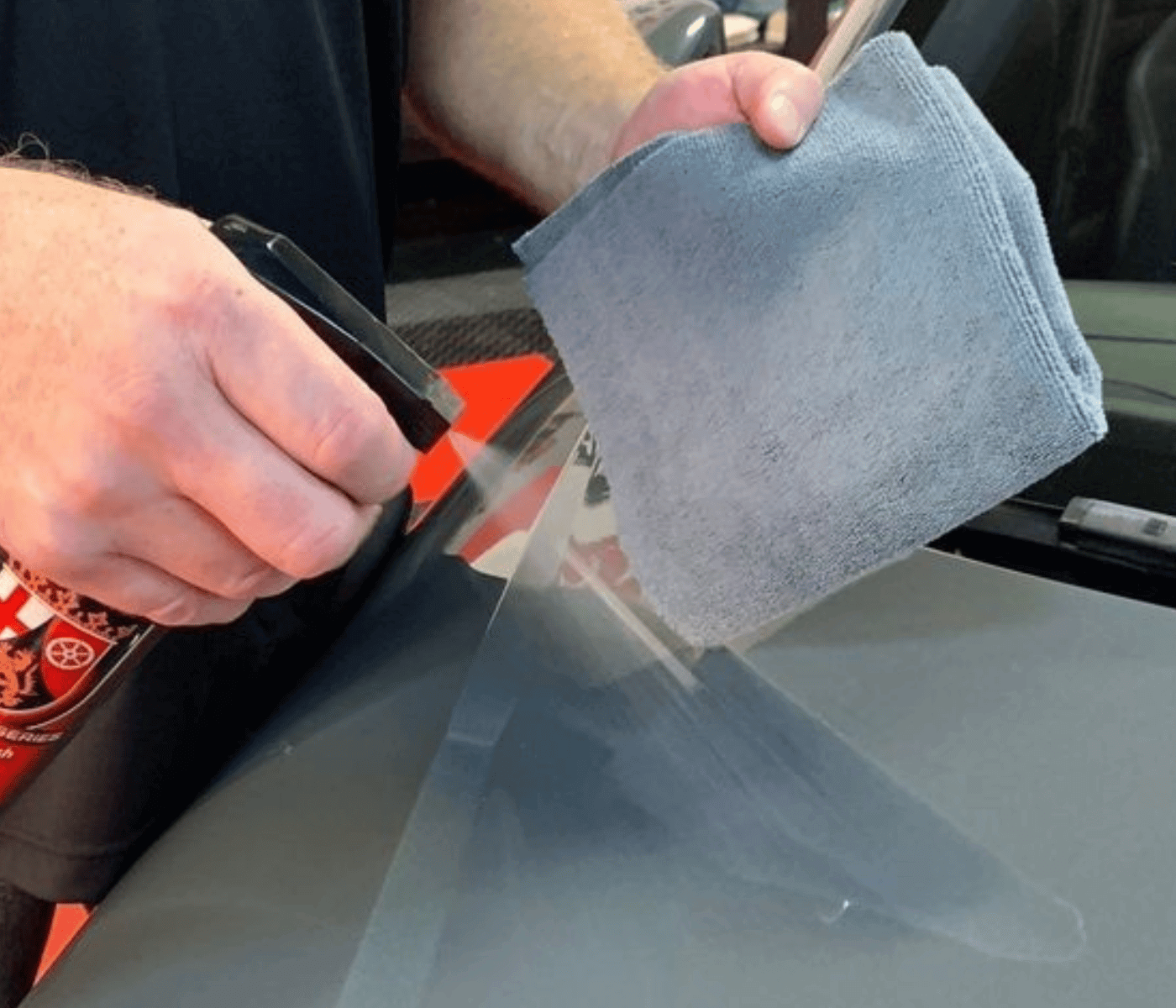 Man spraying paint sealant booster on grey car while holding a grey microfiber applicator towel.