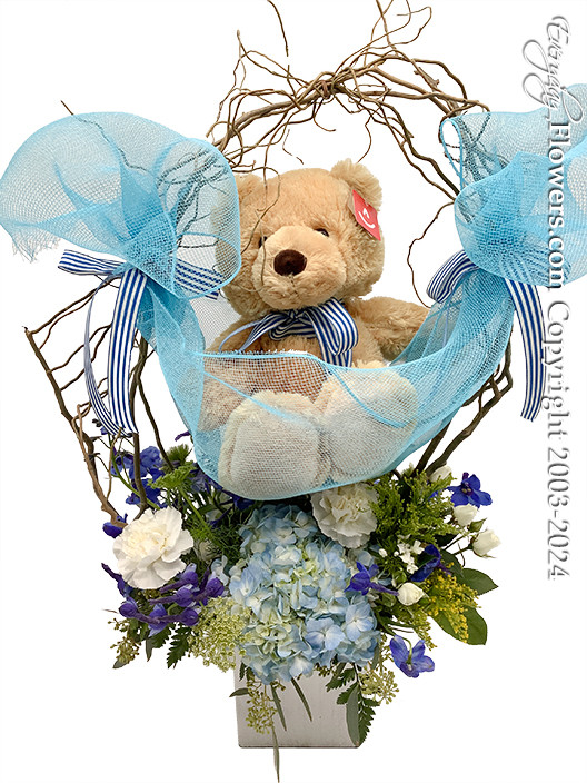 Welcome a New Baby boy by sending a blue and white floral bouquet cradling your choice of stuffed animal by hanging blue fabric mesh across curly willow.