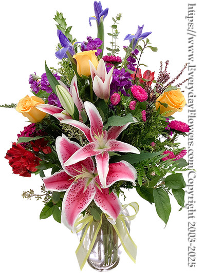 A large 11" Tall Glass Vase filled with Stargazer Lilies, Yellow Roses, Pink Asters, Red Alstroemeria, Purple Hoary Stock, Blue Iris and Seasonal Filler Flowers finished with a Yellow Hand Tied Bow.