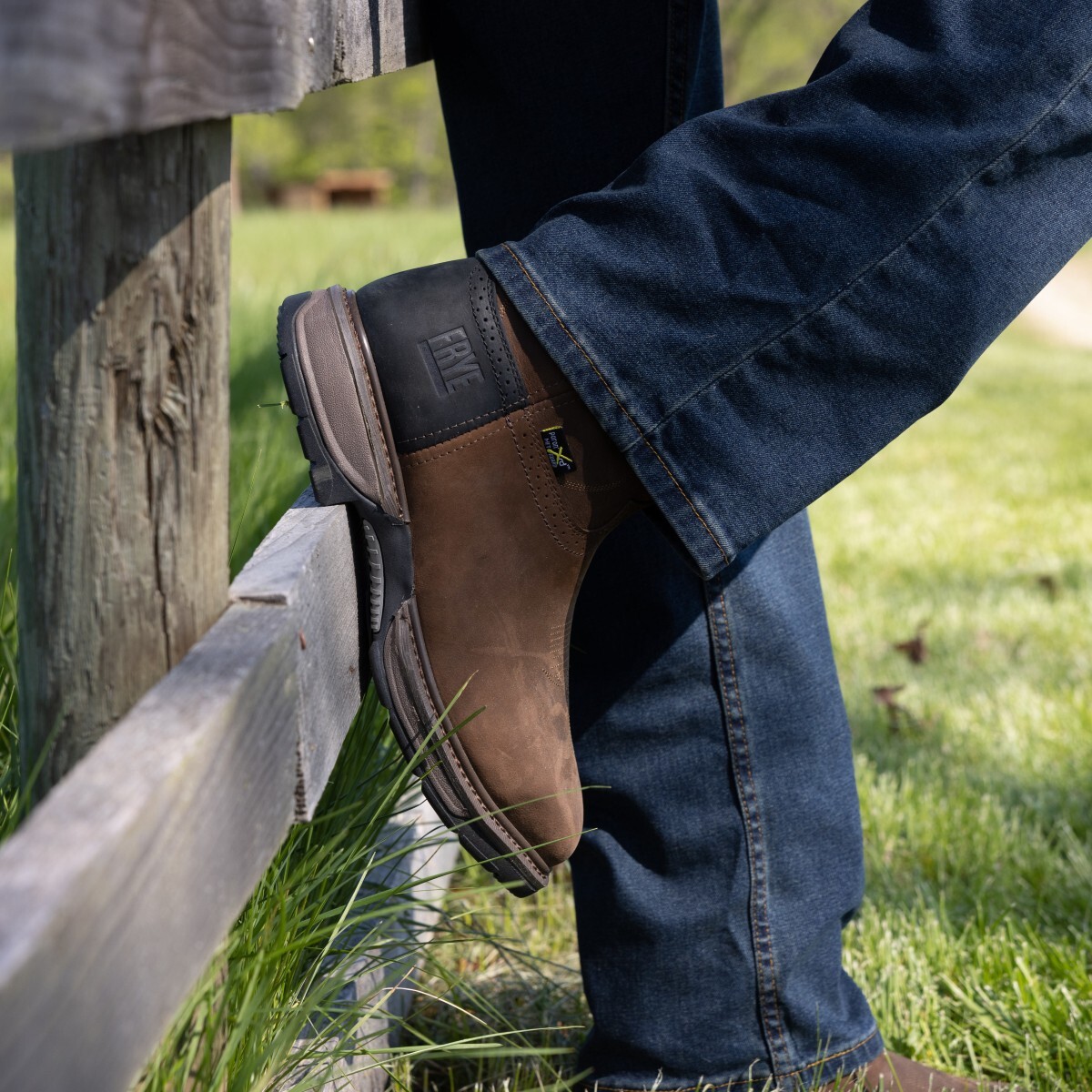 Man wearing western work boots in style FR40101 with foot propped up against a wooden fence.