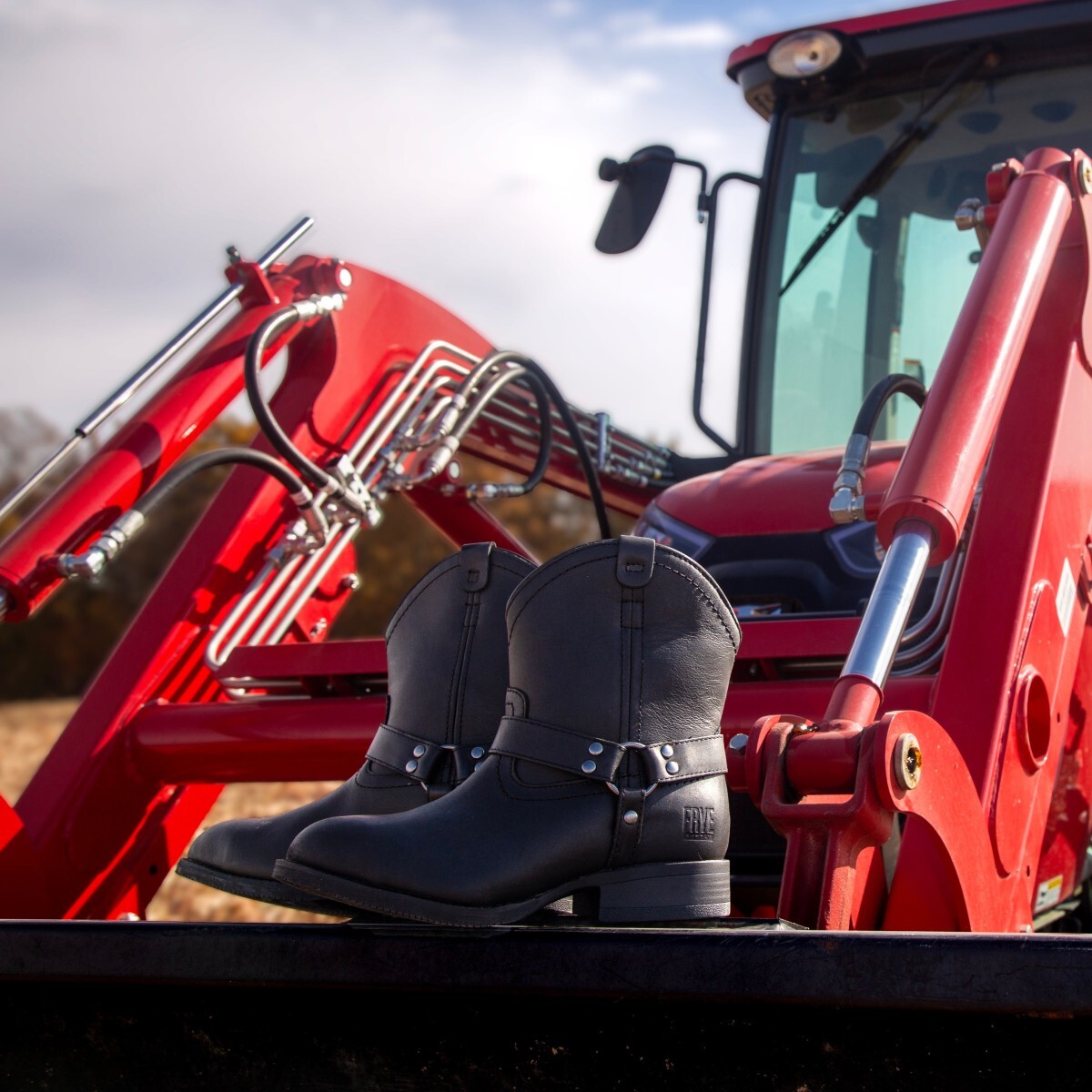 fr40601f-harnessboot-frye-supply-img-7679-square.jpg Women’s harness farm boots sitting on the edge of a red tractor’s bucket.