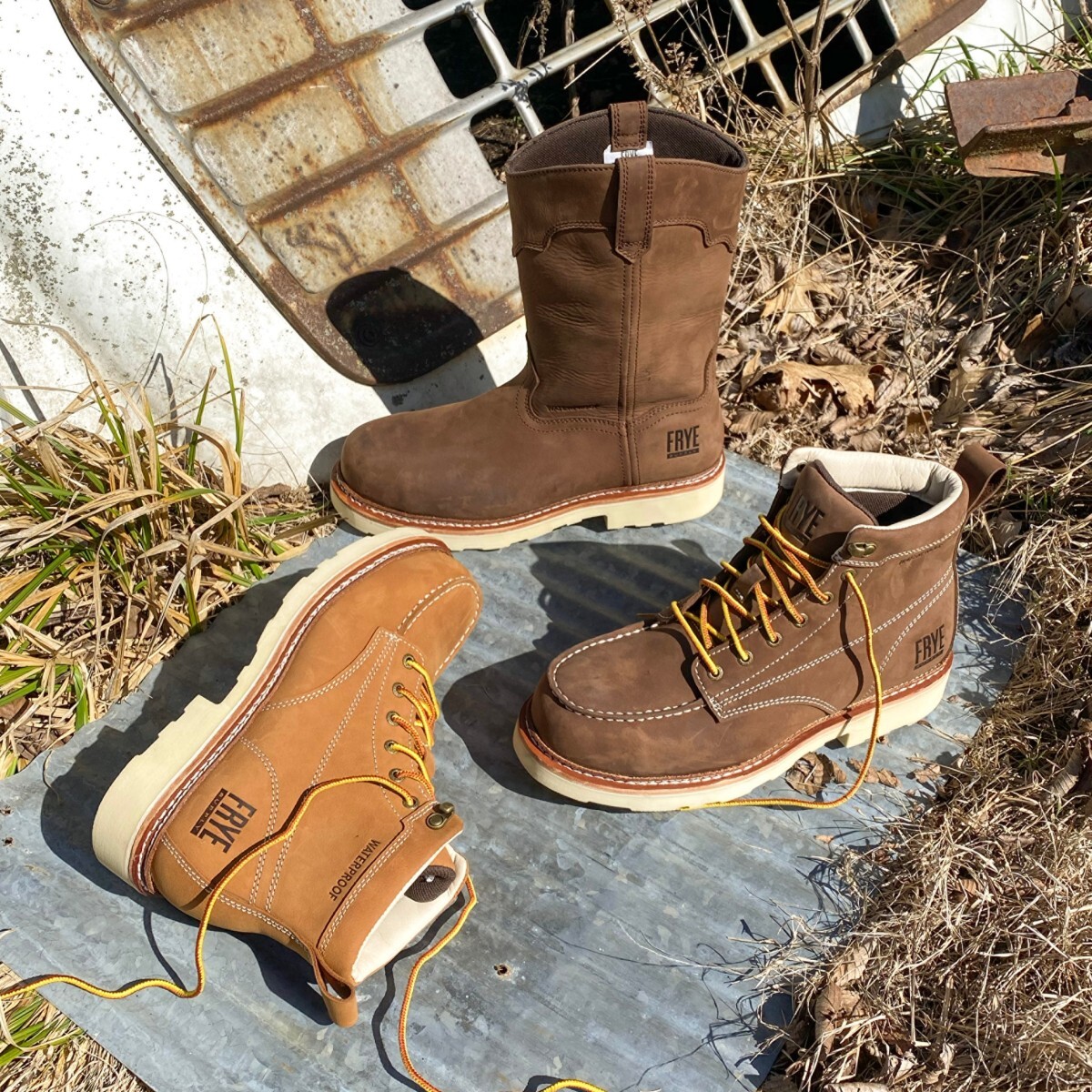Three pairs of Frye Supply work boots posed sitting on sheet metal on hay