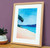 Beach print framed in slim warm oak frame, placed on a sideboard.