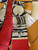 The image shows a Louis Vuitton scarf with a distinctive design. The scarf features a combination of red and beige colors, with the beige sections adorned with the classic Louis Vuitton monogram pattern. The design also includes artistic illustrations of what appear to be Louis Vuitton bags. The brand name "LOUIS VUITTON" is prominently displayed on the red section of the scarf. The scarf is placed on a white fur surface, with a Louis Vuitton box and a receipt partially visible in the background