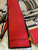 The image shows a Louis Vuitton scarf with a distinctive design. The scarf features a combination of red and beige colors, with the beige sections adorned with the classic Louis Vuitton monogram pattern. The design also includes artistic illustrations of what appear to be Louis Vuitton bags. The brand name "LOUIS VUITTON" is prominently displayed on the red section of the scarf. The scarf is placed on a white fur surface, with a Louis Vuitton box and a receipt partially visible in the background