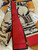 The image shows a Louis Vuitton scarf with a distinctive design. The scarf features a combination of red and beige colors, with the beige sections adorned with the classic Louis Vuitton monogram pattern. The design also includes artistic illustrations of what appear to be Louis Vuitton bags. The brand name "LOUIS VUITTON" is prominently displayed on the red section of the scarf. The scarf is placed on a white fur surface, with a Louis Vuitton box and a receipt partially visible in the background