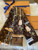 The image shows a Louis Vuitton Monogram Confidential Bandeau Scarf, model number M78655. The scarf features the iconic Louis Vuitton monogram pattern in brown with various illustrations of chains, locks, and belts in gold and beige tones. The Louis Vuitton logo and the text "Louis Vuitton Paris" are prominently displayed on the scarf. The scarf is new and comes in its original box, which is partially visible in the background. Additionally, there is a tag attached to the scarf with a barcode and the model number M78655