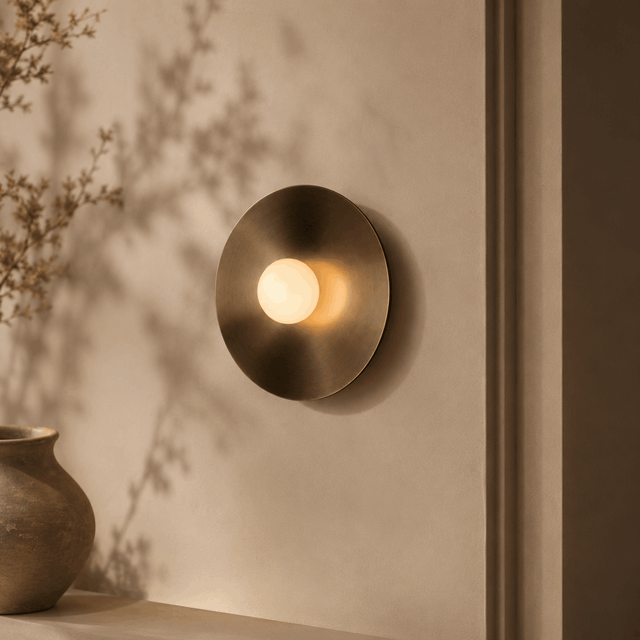 Oria Brass Wandleuchte mit runder Scheibe in Messing-Optik und Glaskugel an heller Wand