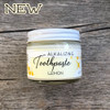 Photo of lemon toothpaste with graphic reading "new" on wooden background glass jar with white metal lid