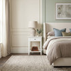 White Hampstead 1 Drawer Bedside Side Table beside an upholstered bed, styled with a ceramic lamp, decorative bowl and greenery in a bright contemporary bedroom.