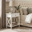 Hampstead 1 Drawer Bedside Side Table in white styled beside a bed with a ceramic lamp, eucalyptus vase and open shelf with stacked books in a modern Hamptons bedroom.