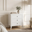 Piastri 3 Drawer Bedside Table in White showcasing its hand-finished white patina, carved moulding, antique bronze handles and spacious drawers with timeless Hamptons-inspired style.