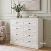 Hamptons style white wooden dresser against pale grey wainscoting.