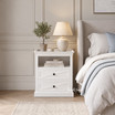 Hamptons style white bedroom nightstand set against pale paneled wainscoting.