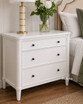 Detailed view of a white three drawer side table, showing three generous drawers and simple detailing.