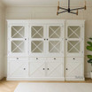 Somerset 4 Door Display Wall Unit in situ in living room, highlighting its Hamptons-inspired design, signature cross detailing on the doors, and spacious shelving, perfect for use as a display unit or bookshelf.