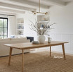 Wide view of a contemporary light oak dining table with tapered leg in a styled modern Hamptons-inspired living room setting