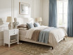 Lando 1 Drawer white bedside table paired with a fabric bed and soft blue accents in a light-filled Hamptons bedroom interior.