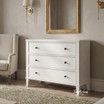 White Lando 3 Drawer Chest styled beneath a gold framed mirror in a contemporary living room, showcasing spacious storage, classic panel detailing and bronze knobs.