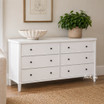 A styled front angled view of the Brynmore 6 Drawer Chest in White, an elegant storage option for either living room or bedroom spaces.