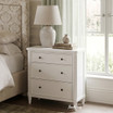 Thomas and Hurley Brynmore white petite nightstand positioned next to an upholstered bed near a bright window.