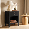 Black side table with framed drawer and generous lower shelf styled with a lamp and round timber side table