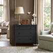 Wide black bedside cabinet with classic detailing and tapered legs in a styled living room with natural light and wainscoting