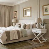White Hampstead Cross Leg Bedside Side Table with single drawer and classic cross-leg base styled with a ceramic lamp, books and floral arrangement.