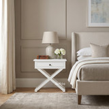 White Hampstead Cross Leg Bedside Side Table featuring a single drawer and signature cross-leg design beside an upholstered bed with neutral bedding.