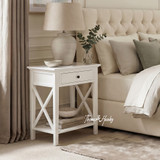 Hampstead 1 Drawer Bedside Side Table in white styled beside a bed with a ceramic lamp, eucalyptus vase and open shelf with stacked books in a modern Hamptons bedroom.