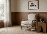 The elegant curved lines and cabriole legs of the hand-crafted Cannes Weathered Oak Armchair in a warm minimalist living room styled with art and a side table