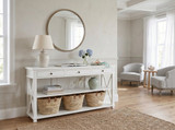 White Hampstead 3 Drawer Console with Shelf styled in a bright coastal entryway with a round mirror, table lamp, decorative baskets and home accessories.